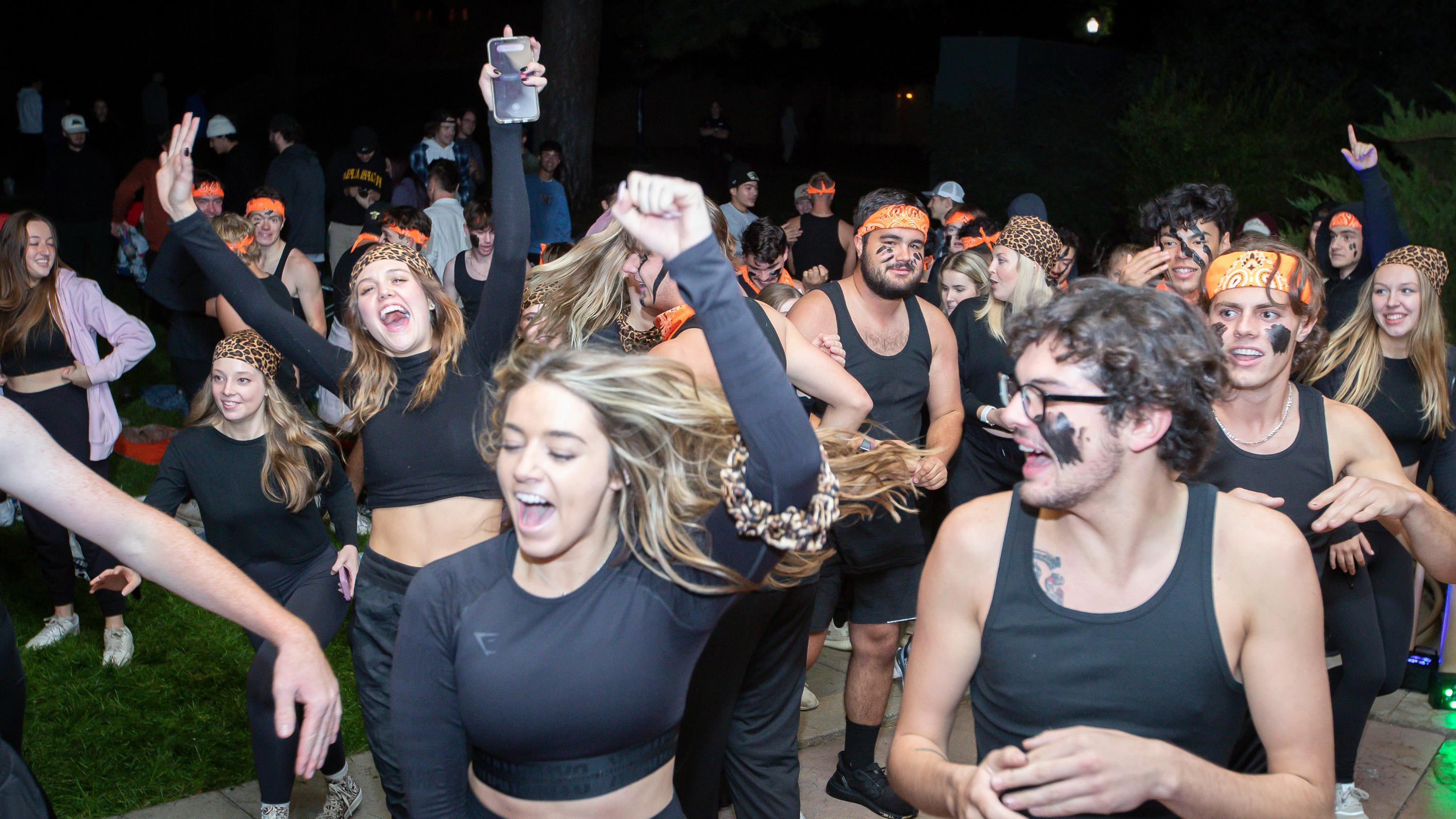 Fraternity and sorority members dressed in black and orange dancing together