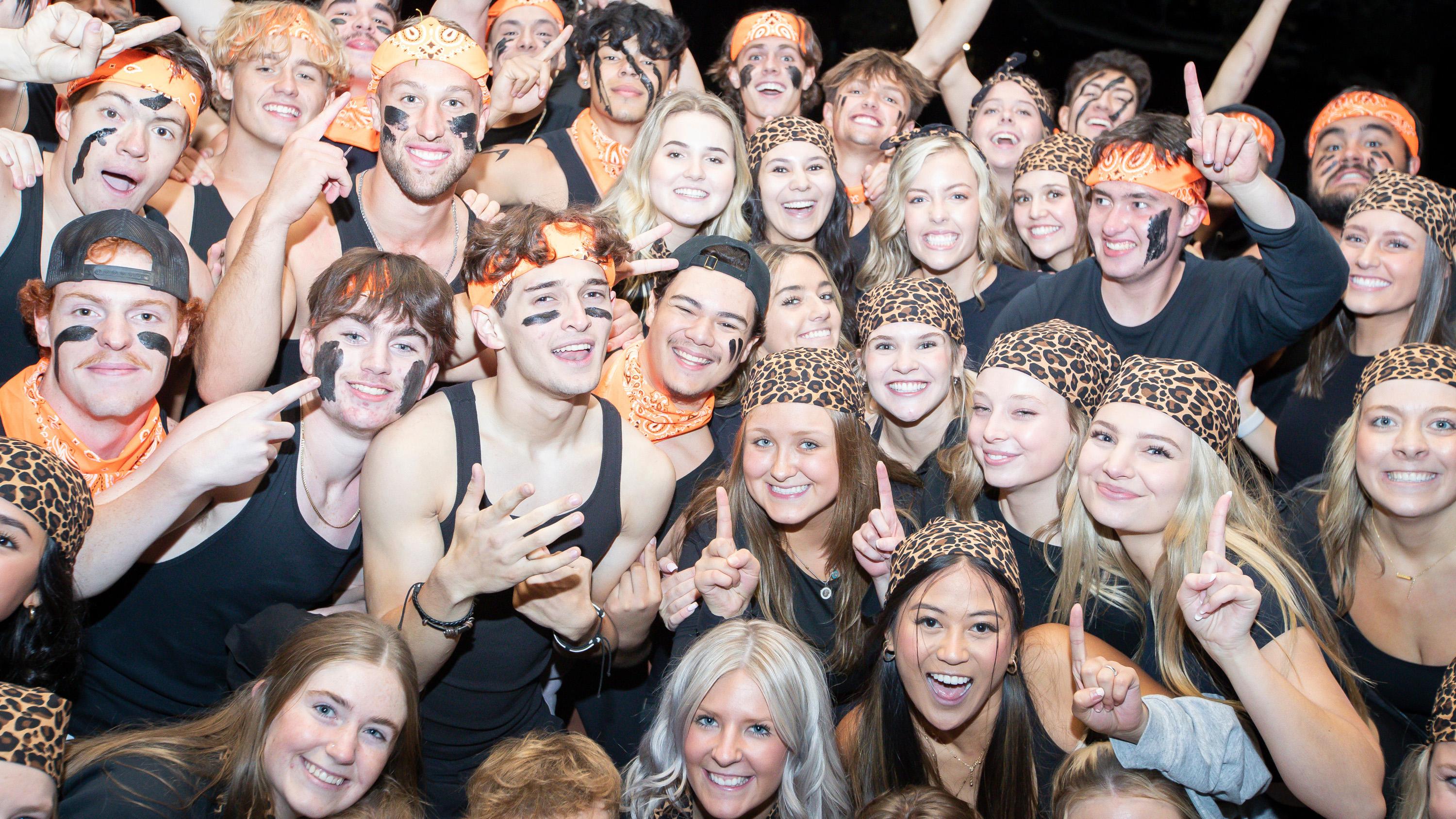 A large number of students wearing black and orange huddled together smiling