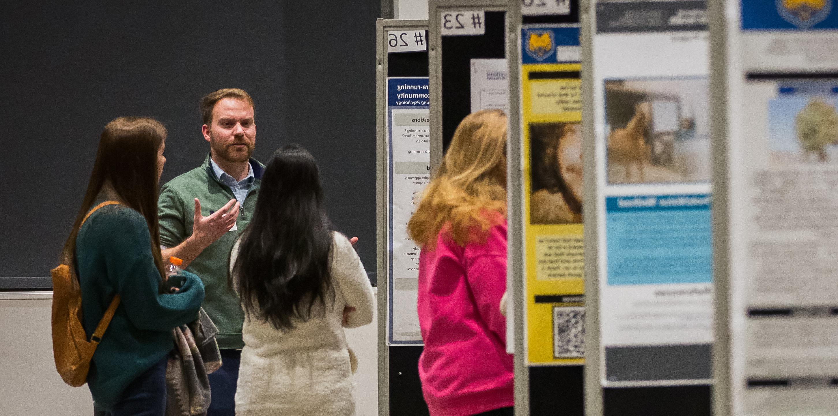 a group of students standing and talking in front of several research posters 