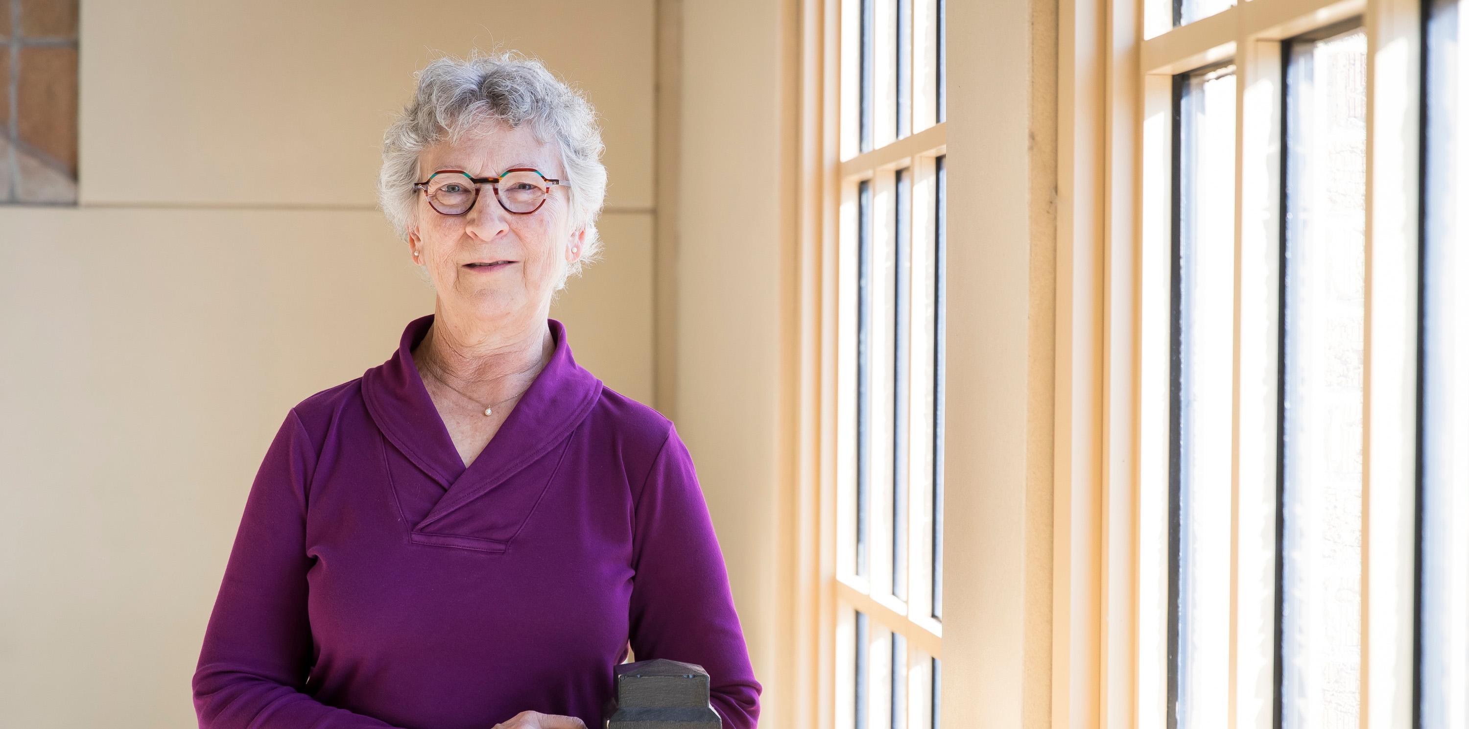 Liz Kissell leaning on a railing near windows smiling