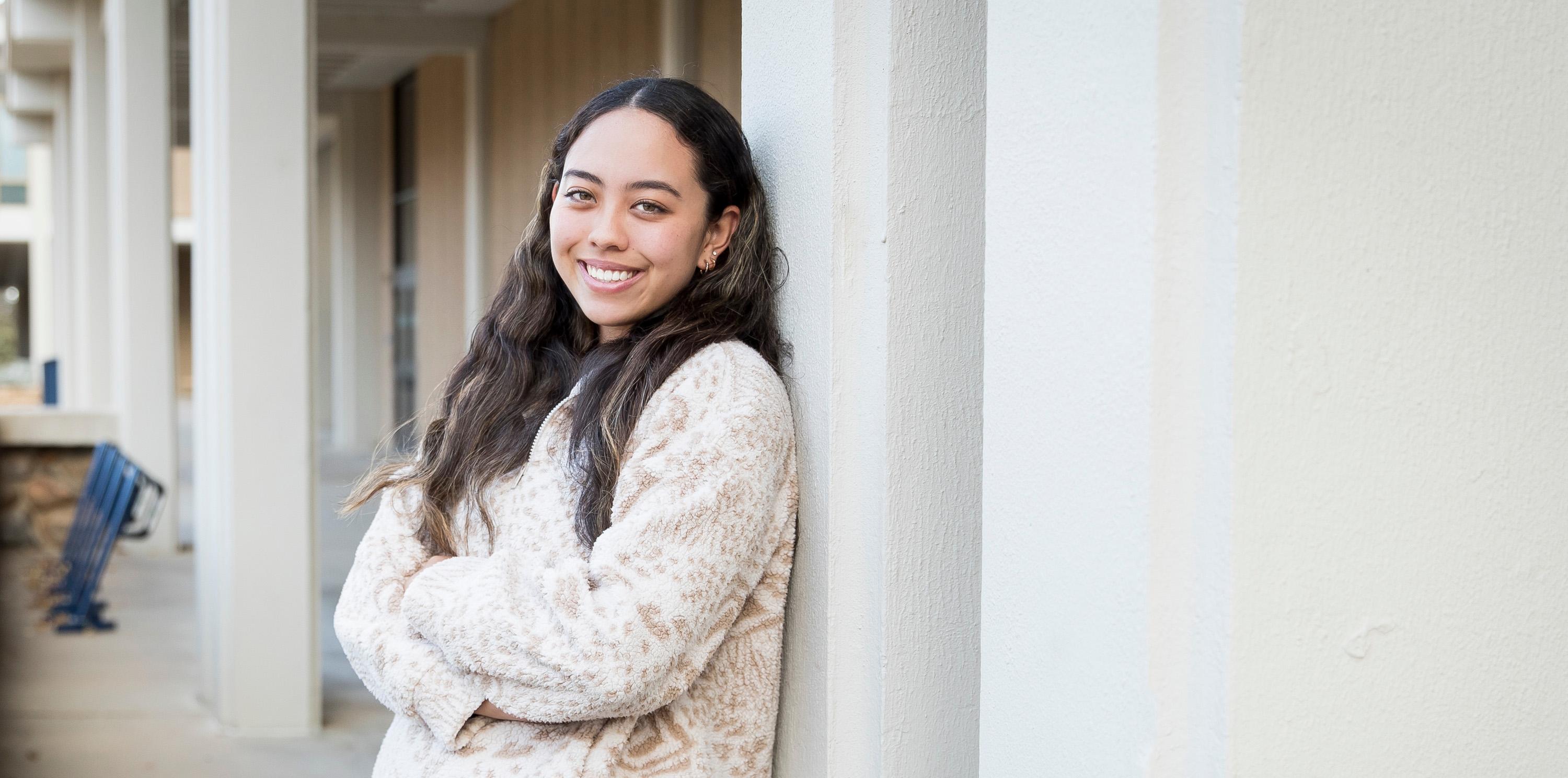 Female student, Shae Lefcourt smiling and leaning on a building on UNC's campus